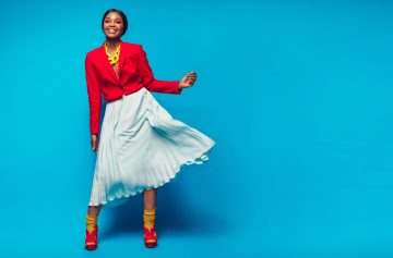 Full length shot of attractive woman in beautiful dress. African female fashion model standing over blue background with copy space.